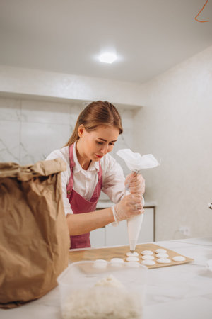 Woman confectioner in kitchen interior fills confectionery bag with freshly prepared cream. Cooking,...