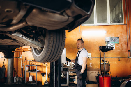 Young car mechanic at repair service station inspecting car wheel and suspension detail of lifted automobile. Bottom view. High quality photoの写真素材