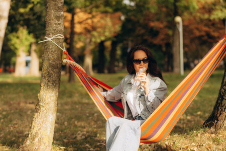 Young lovely woman relaxes on a hammock and drinks cold water with mint and lemon. High quality...