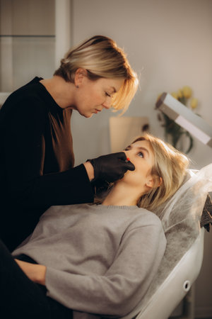 Face of girl in profile during microblading permanent makeup process. Hands of tattoo master holding professional ink machine with medicine needle. High quality photoの写真素材