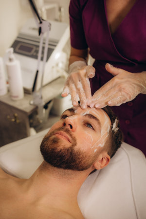 Cosmetologist applying mask on man's face in spa salon, top view. High quality photoの写真素材