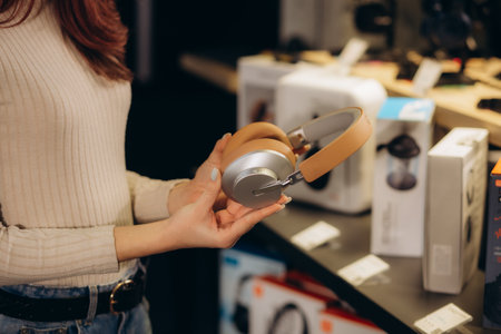girl standing in front of the stand in the electronics store chooses headphones before buying wearing on her head listening to the sound. High quality photoの写真素材