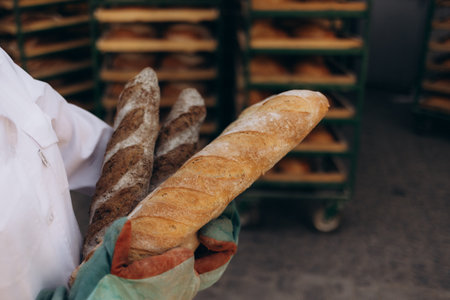 Close up of baker is taking off from oven the french baguette bread with wood peel at baking manufacture factory. French baguette bread bakery factory concept.の写真素材