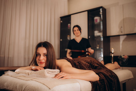 Masseur makes massage to young girl. Woman having bamboo stick massage at day spaの写真素材