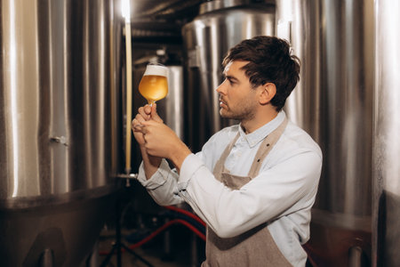 Brewery worker looking at freshly made beer in glass mugの写真素材