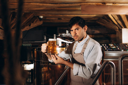 Young man examining the quality of craft beer at brewery. Male inspector working at alcohol...