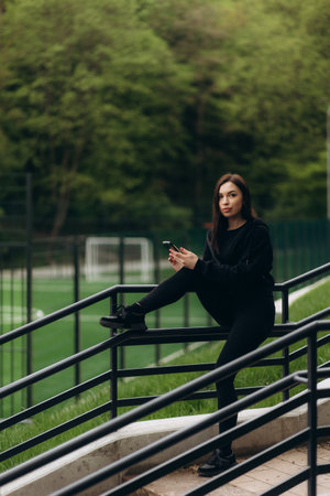 Caucasian girl in sport outfit is smiling and using her smart phone in a green park.の写真素材