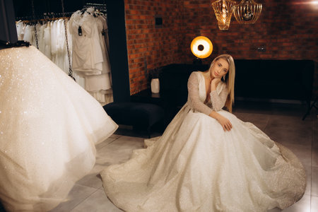 Smiling pretty bride chooses white gown at shop of wedding fashionの写真素材