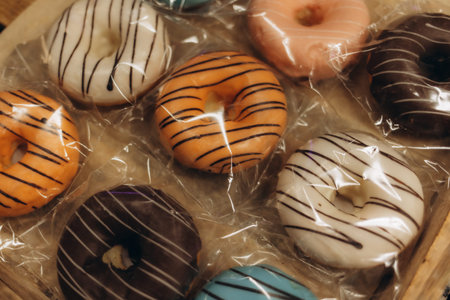 Ten colorful donut in the plastic box. One of donut already bitted and tasted.
