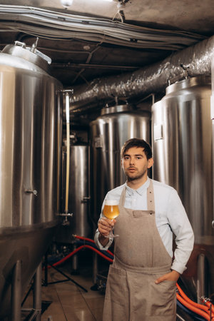 Young man examining the quality of craft beer at brewery. Male inspector working at alcohol manufacturing factory checking the beer.の写真素材