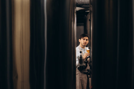 Young man examining the quality of craft beer at brewery. Male inspector working at alcohol manufacturing factory checking the beer.の写真素材