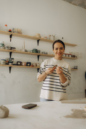 Serious creative female artisan standing at pottery workshop and making clay mug. Portrait of a focused artistic craftswoman standing at ceramics studio and making earthenware.Artisan making clay mug.の写真素材