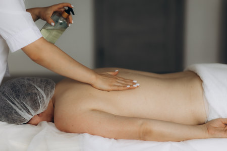 Closeup of masseur hands pouring aroma oil on woman back. Masseuse prepare to do oriental spa procedure for relaxing treatment. Therapist doing aromatherapy oil massage on woman body.の写真素材