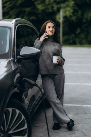 Woman charging electro car and talking on the phoneの写真素材