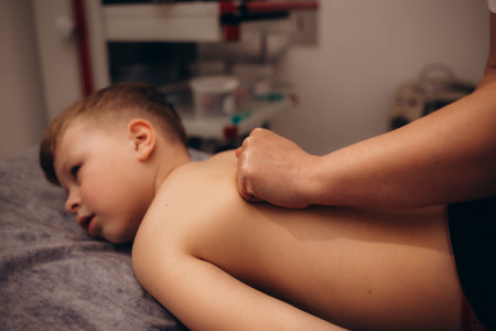 A little boy relaxes from a therapeutic massage. Male massage therapist makes a medical massage to the back of a childの写真素材