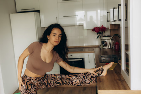 Sporty young woman with healthy smoothie and laptop sitting on yoga mat in kitchenの写真素材