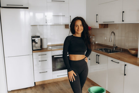 Woman in black sportswear in the kitchen with a yoga mat in her handsの写真素材
