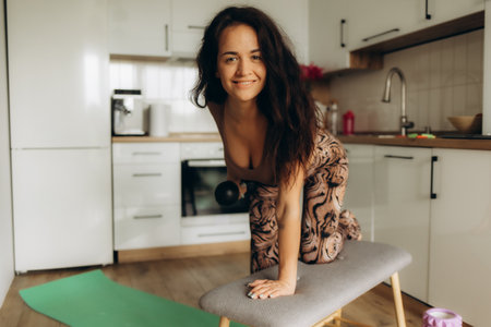 Sporty beautiful mature woman practicing yoga and stretching in kitchen at homeの写真素材
