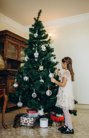 Little girl decorating christmas tree with toys and baubles. Cute kid preparing home for xmas celebration.の写真素材