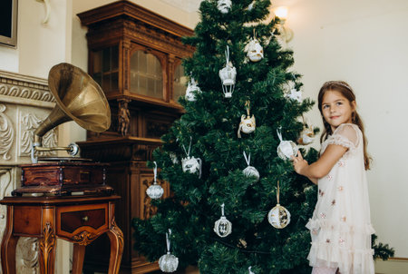 a little girl in a white dress decorates a Christmas treeの写真素材
