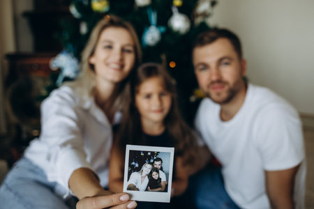 Merry Christmas. Happy mother, father, and kids near Christmas tree in home. Mom, dad hug children. Beautiful family enjoying their holiday time together and having fun. Decorated interior of a house.の写真素材