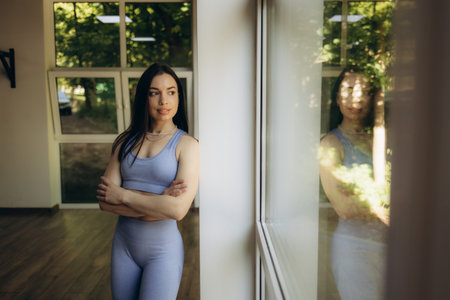 Fit sporty young lady with white towel on neck standing near window looking away, free copy spaceの写真素材