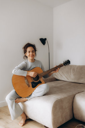 Creative hobby. Talented young mixed race female musician sit in armchair alone compose instrumental song using classic guitar. Smiling biracial lady play calm melody on musical instrument. Copy spaceの写真素材
