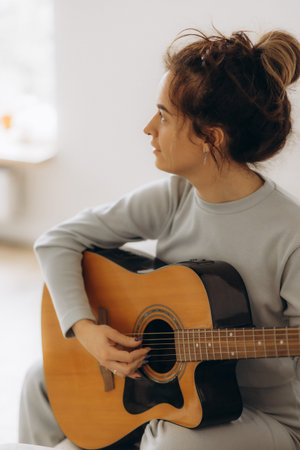Young woman playing guitar in bedroom at home