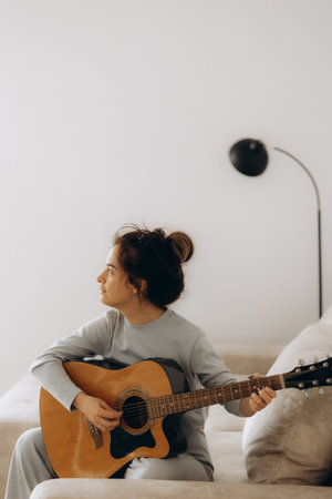 Hobby concept, Young asian woman sitting on couch to singing and playing music with acoustic guitar.