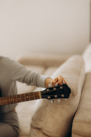 a woman tunes her guitar while sitting on the couchの写真素材