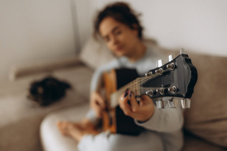 a woman tunes her guitar while sitting on the couchの写真素材