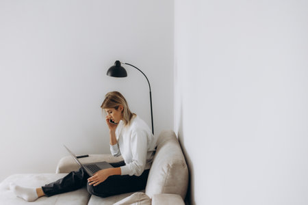 Woman talking on the phone while sitting on the couch with a laptopの写真素材