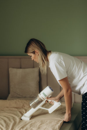 Woman vacuuming the bed in the bedroomの写真素材