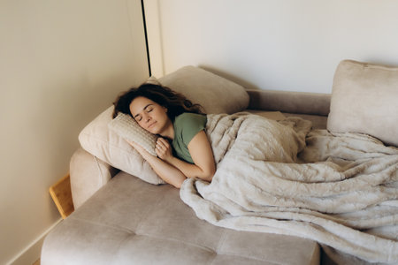 Full length peaceful woman resting under warm blanket on cozy couch in living room, calm young female with closed eyes sleeping, taking nap or daydreaming, lying on soft pillow with hands under cheekの写真素材