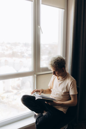Man reading book near window blinds indoors, space for textの写真素材