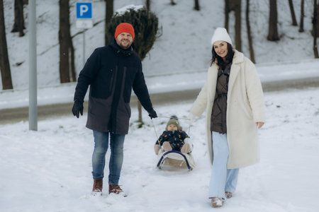 A young family has fun sledding with their son in the winter outdoors