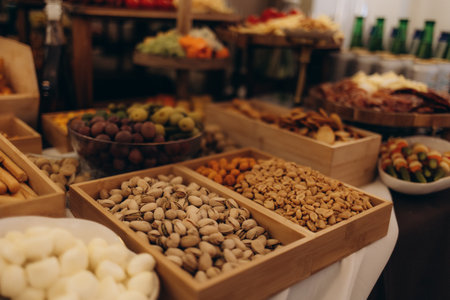 A beautifully arranged charcuterie board featuring an assortment of cheeses, cured meats, crackers, nuts, fruits, and spreads, displayed on a wooden table with serving utensils and dishes.の写真素材