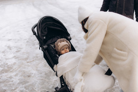 Young mother with a baby carriage in the park during snowfallの写真素材