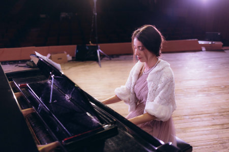 A beautiful woman gracefully playing the piano on stage, dressed in elegant evening attire, under soft spotlight lighting, embodying artistry and sophistication in a concert setting.の写真素材