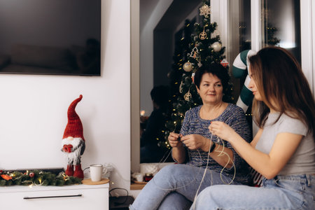 Two women engage in creative holiday decoration activities near a beautifully decorated Christmas tree, reflecting warmth, togetherness, and festive cheer during the holiday season.の写真素材