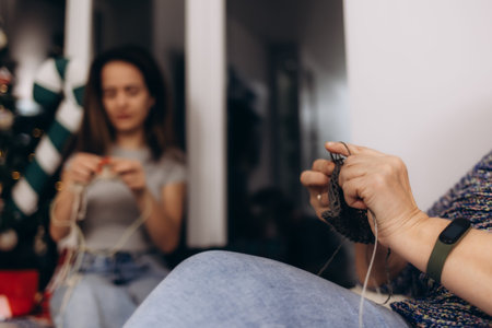 Two women enjoying a knitting activity indoors, with a cozy holiday-themed background, capturing togetherness and creativity during the festive season.の写真素材