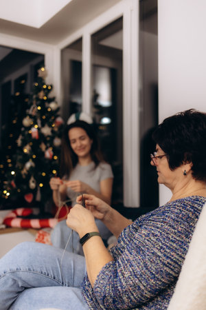 A heartwarming scene featuring generations bonding through knitting, sharing moments of love and tradition near a beautifully decorated Christmas tree. Celebrating family unity and creative pastimes during the festive season.の写真素材