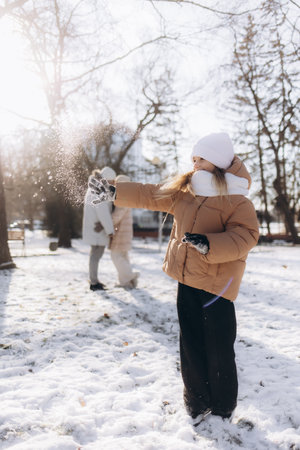 A young woman wearing winter clothing enjoys a snowy day, playfully interacting with the fresh snow in a park while basking in sunlight.の写真素材