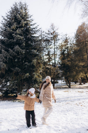 Mother and child enjoying a playful moment together in the snowy outdoors, surrounded by a serene natural environment featuring evergreen trees and winter beauty.の写真素材