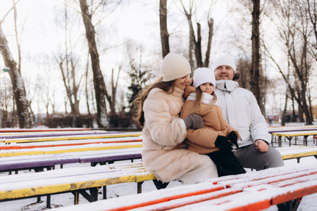 A joyful family seated together during winter, enjoying a scenic snowy park setting. Capturing warmth, unity, and the serene beauty of nature on a crisp, chilly day.の写真素材