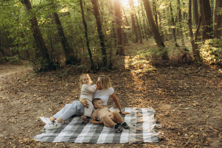A serene moment of a family bonding together while sitting on a blanket in the woods. The image captures the warmth, love, and joy of spending time in the tranquility of nature.の写真素材