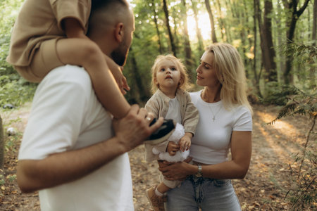 A loving family enjoying nature together in a beautiful forested area. The photo highlights the emotional bond and connection of parents with their children, showcasing warmth, care, and togetherness.の写真素材