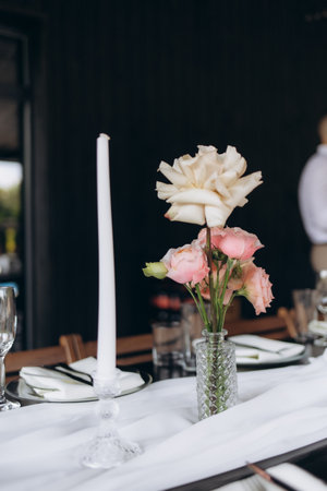 Table decoration with a floral vase arrangement and white taper candle, creating an elegant atmosphere appropriate for celebrations such as weddings, special dinners, or sophisticated gatherings.の写真素材