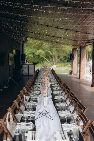 A beautifully arranged long table for a wedding, featuring floral centerpieces, sparkling glasses, and fairy lights creating a magical ambiance in an outdoor setting.の写真素材