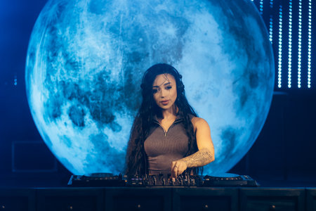 A captivating female DJ focuses on mixing tracks at the DJ console, framed by a glowing full moon backdrop. The ambient lighting creates an electrifying atmosphere of music and energy.の写真素材